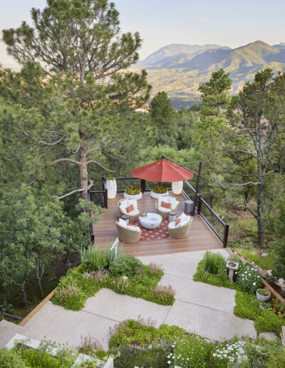 outdoor patio with white cushion chairs, red umbrella and mountain in background, trees around